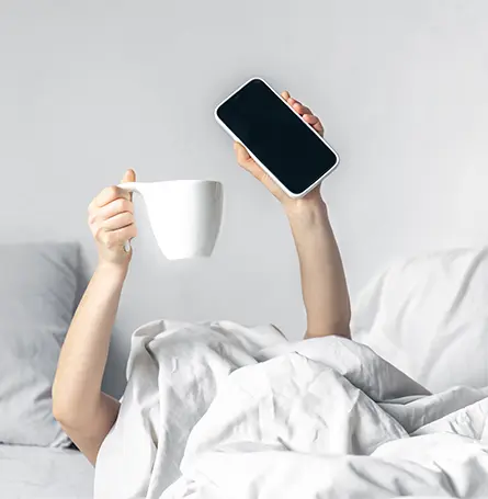 L'image d'une personne au lit tenant un mug et son téléphone.