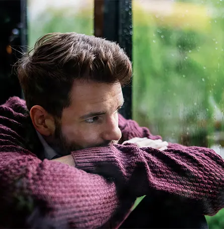 Image d'un homme atteint de dépression saisonnière regardant par la fenêtre