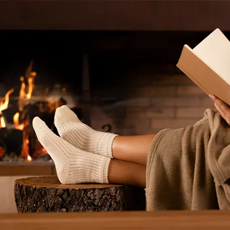 Image d'une personne utilisant une couverture électrique et lisant un livre devant une cheminée.