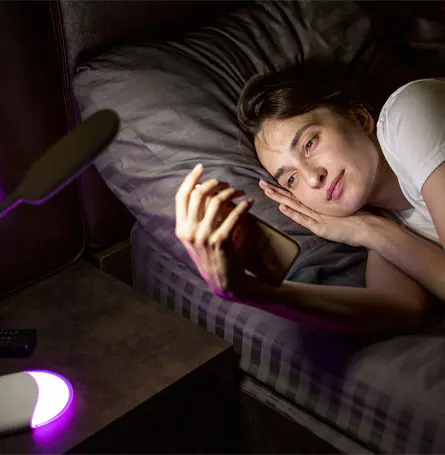 Image d'une femme regardant son téléphone dans son lit, la lumière frappant son visage.