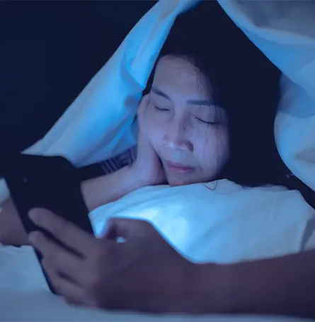 Image d'une femme au lit regardant son téléphone